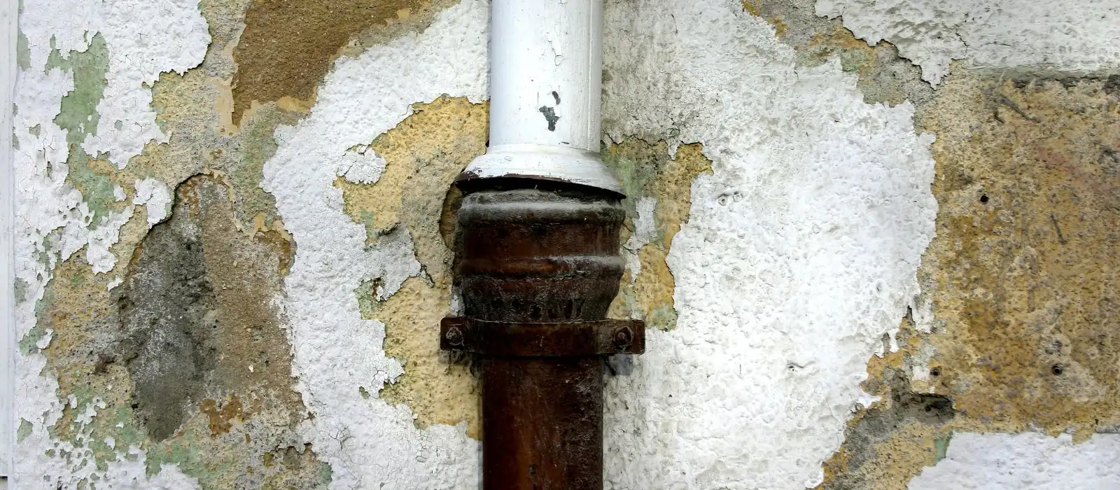 Peeling plaster and stained wall around a drain pipe